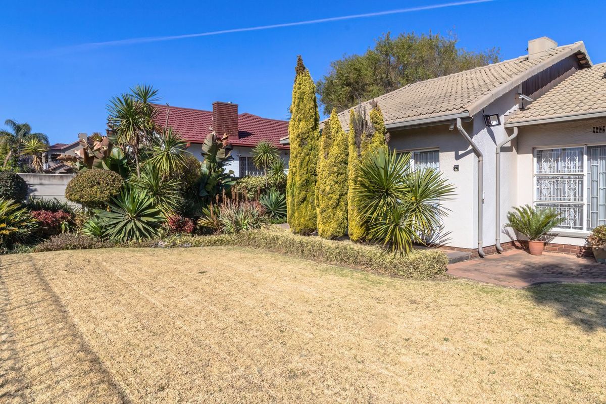 Rear view of the property featuring a paved patio area, established garden landscaping, and a tiled roof with solar water heating infrastructure.