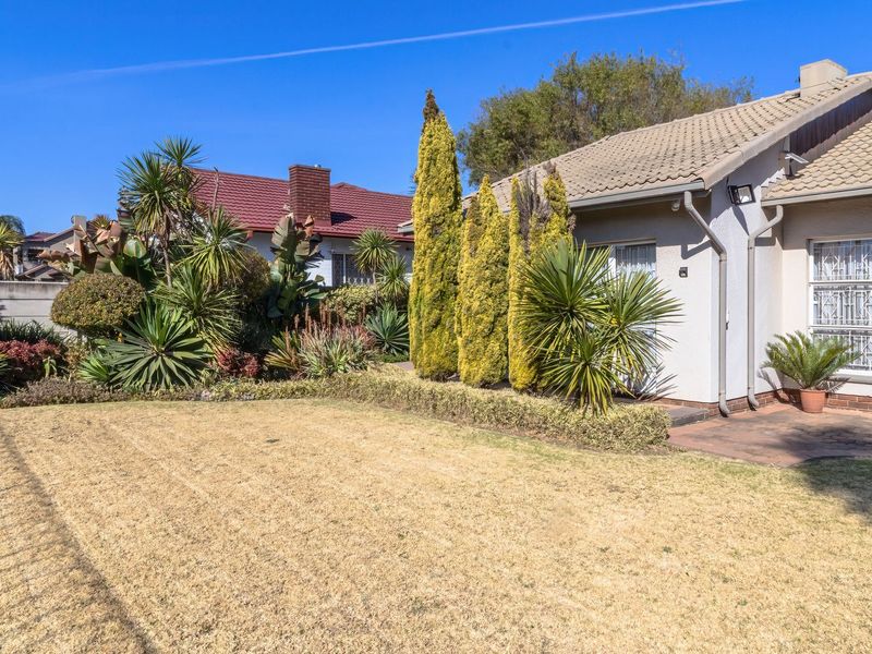Rear view of the property featuring a paved patio area, established garden landscaping, and a tiled roof with solar water heating infrastructure.