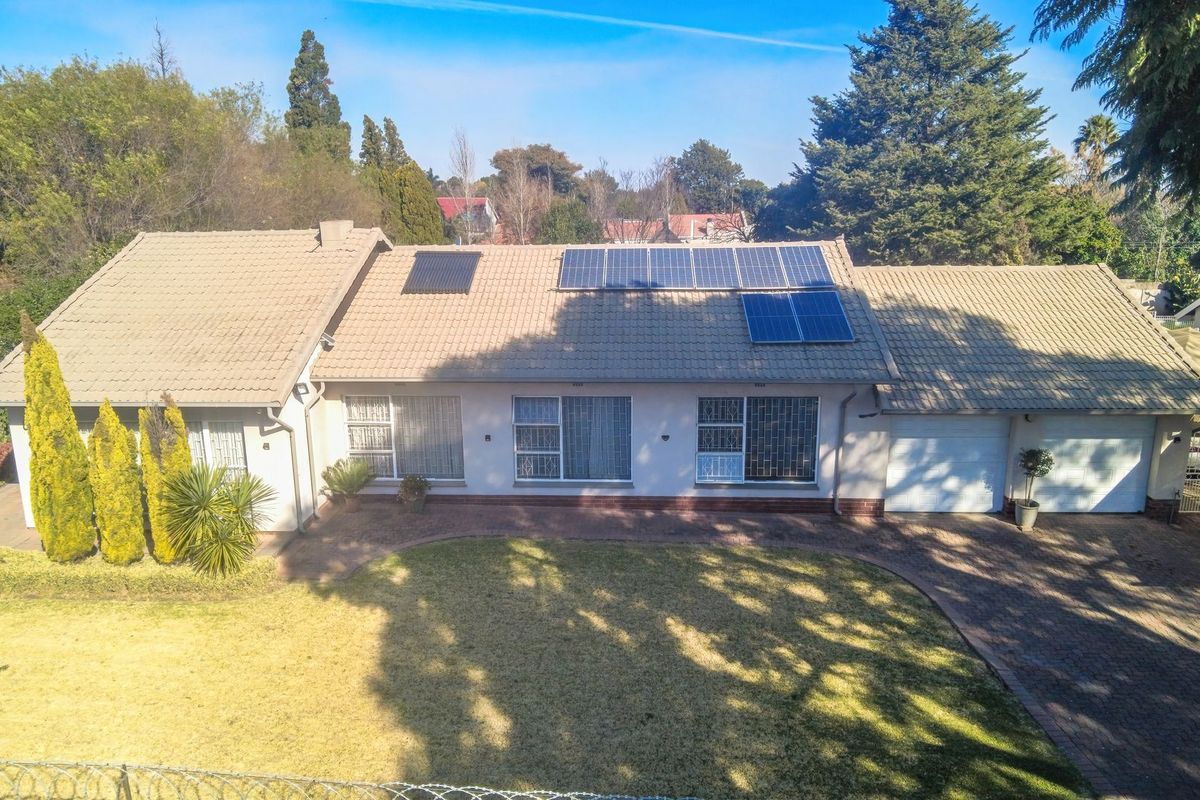 Aerial view of a single-story residential property featuring a tiled roof with solar panels, a paved driveway, and a double garage.