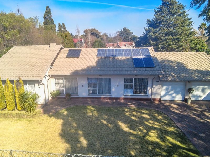 Aerial view of a single-story residential property featuring a tiled roof with solar panels, a paved driveway, and a double garage.