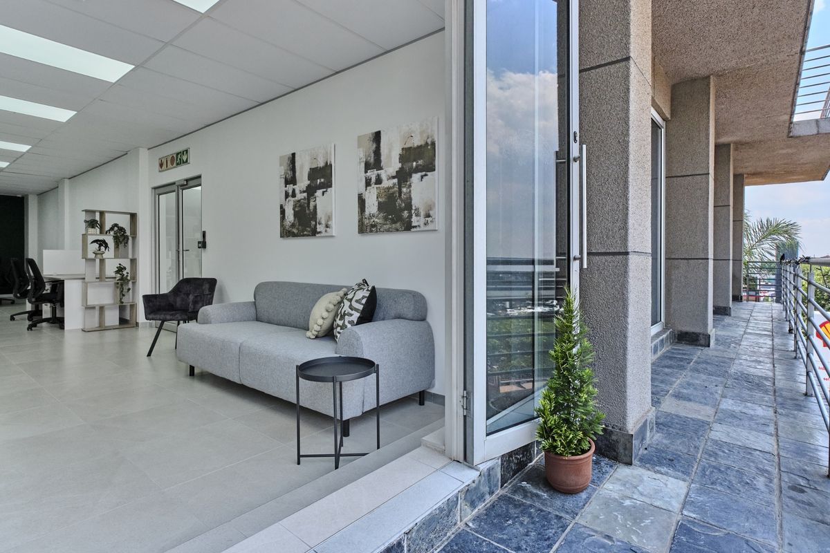 Modern open-plan office space featuring neutral tiled flooring, suspended ceilings, and large bi-fold glass doors opening onto a stone-tiled balcony.