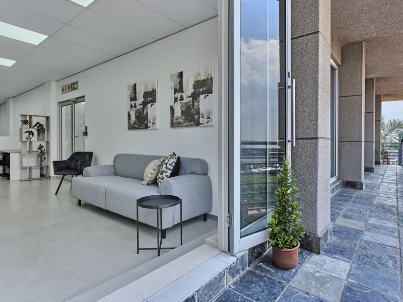 Modern open-plan office space featuring neutral tiled flooring, suspended ceilings, and large bi-fold glass doors opening onto a stone-tiled balcony.