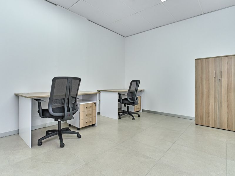 A clean, professional office space featuring neutral tiled flooring, a suspended ceiling, and functional built-in storage cabinetry.