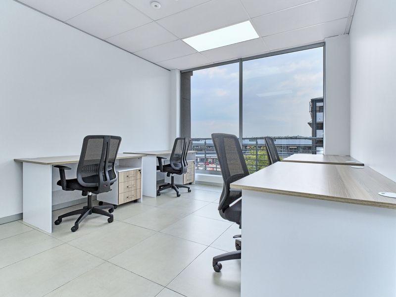 A bright, modern office space featuring large floor-to-ceiling windows, tiled flooring, and a suspended ceiling with recessed lighting.