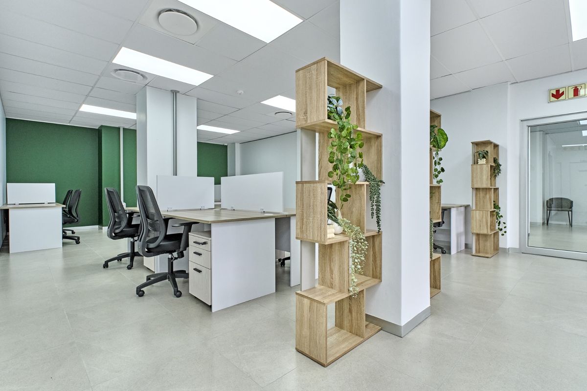 Modern open-plan commercial office space featuring tiled flooring, recessed ceiling lighting, structural columns, and a glass partition door.