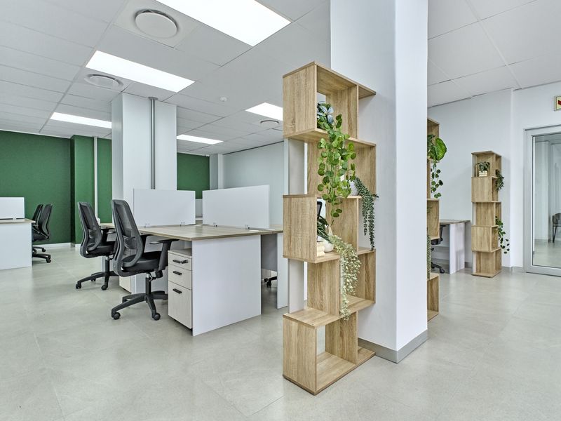 Modern open-plan commercial office space featuring tiled flooring, recessed ceiling lighting, structural columns, and a glass partition door.