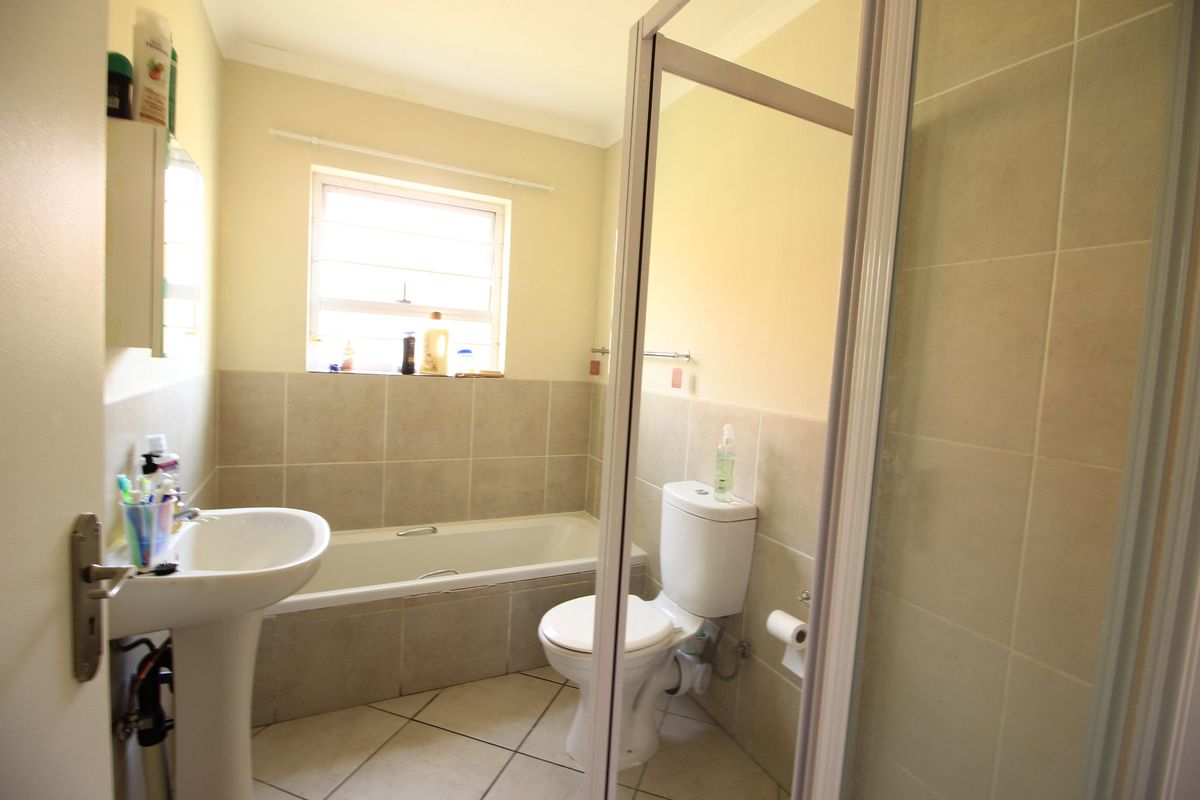 A functional bathroom featuring a pedestal basin, bathtub, toilet, and a separate shower enclosure with neutral wall and floor tiling.