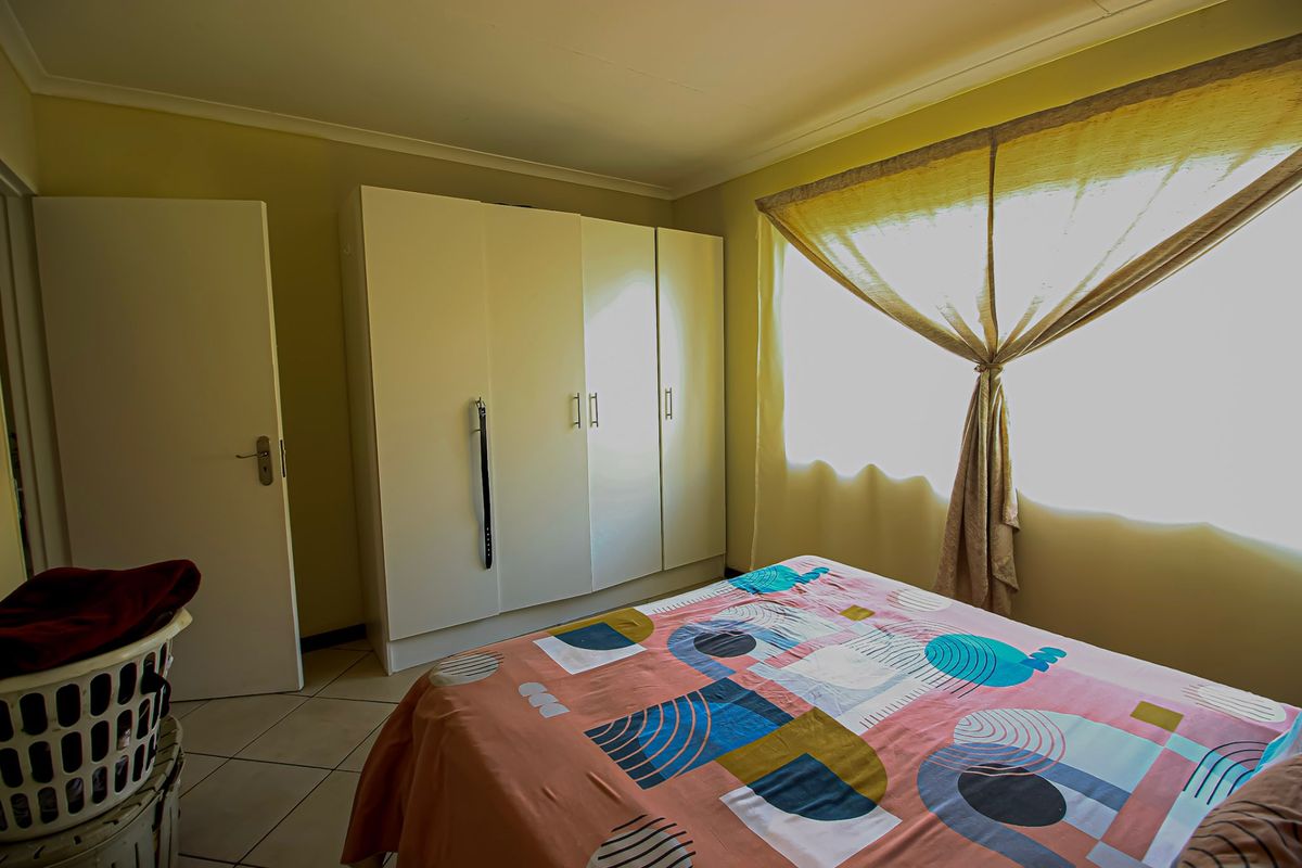 A functional bedroom featuring built-in cupboards, tiled flooring, and natural light through a window with curtaining.