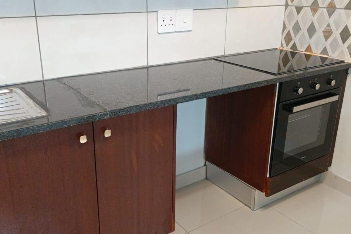 A functional kitchen area featuring dark granite countertops, built-in oven, ceramic hob, and tiled backsplash with neutral cabinetry.