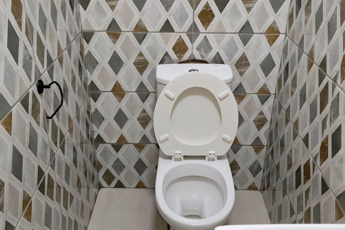 A compact bathroom featuring a modern toilet and decorative diamond-patterned wall tiling throughout.