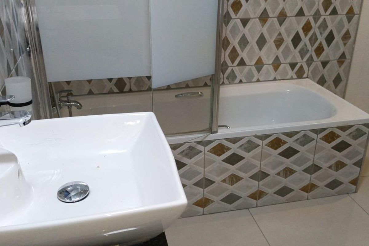 A modern bathroom featuring a vessel sink with chrome faucet, a bathtub with a glass shower screen, and decorative diamond-patterned wall tiling.