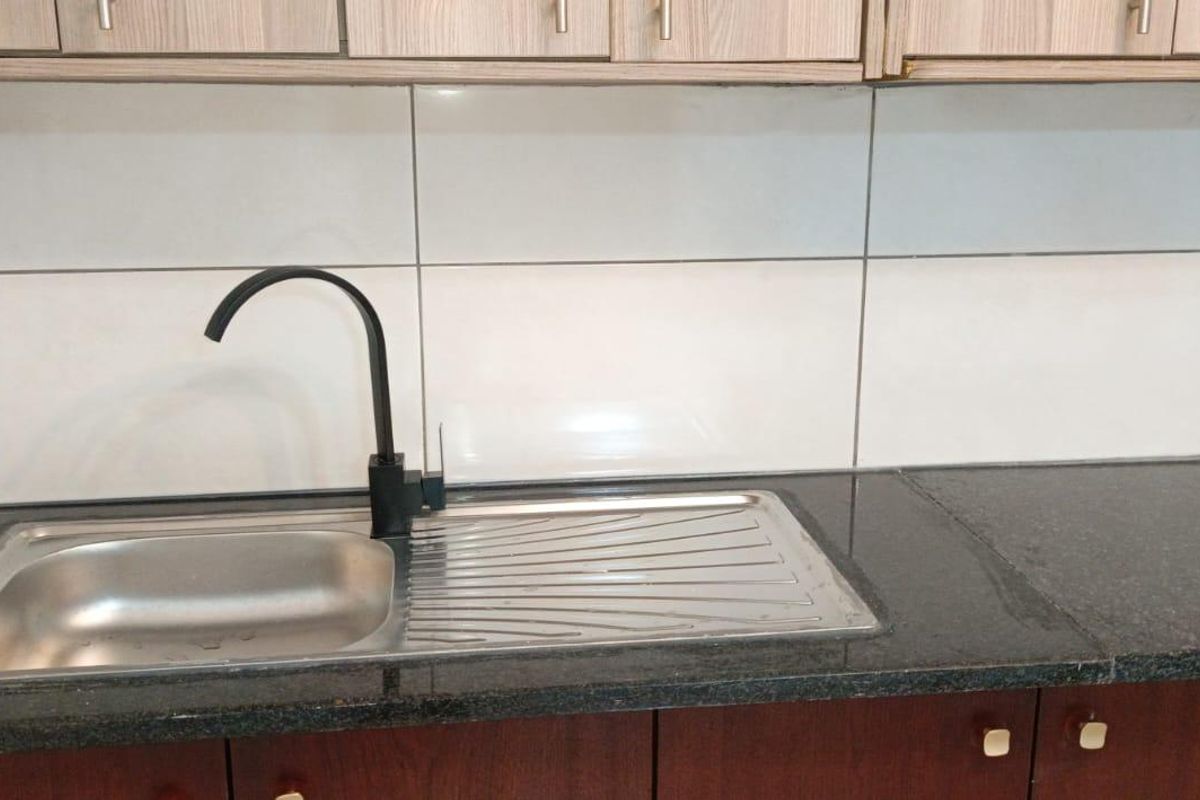 A clean kitchen area featuring a stainless steel sink with a modern black faucet, granite countertops, and tiled backsplash with overhead cabinetry.