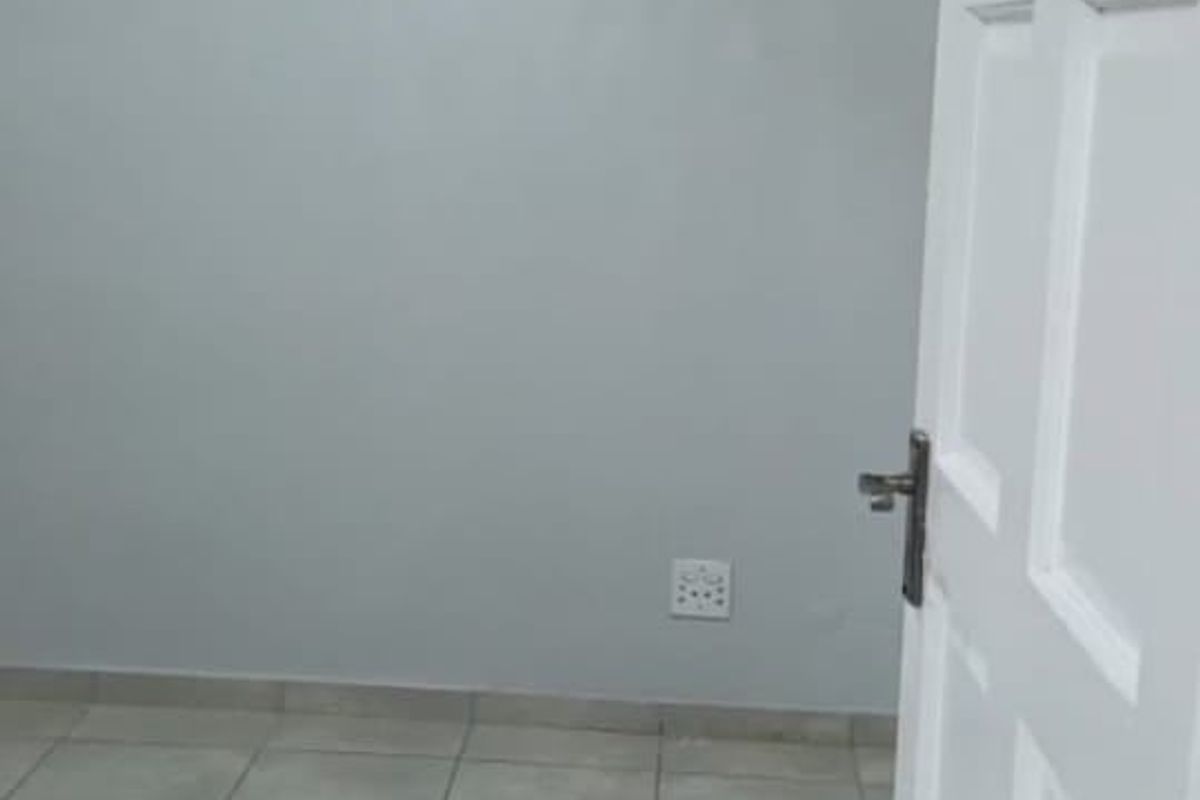 A clean, empty bedroom featuring neutral grey walls, tiled flooring, and a white panel door, providing a blank canvas for personalization.