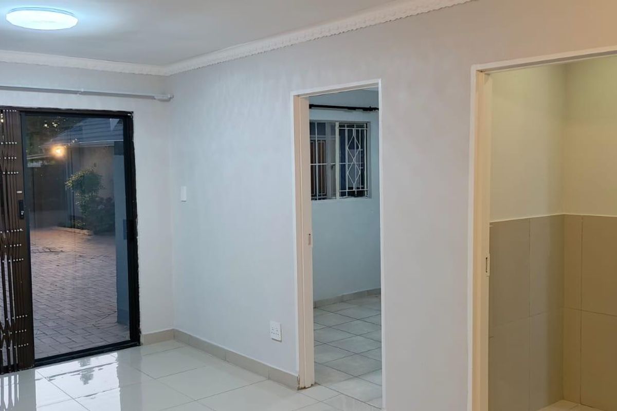 An empty living area featuring tiled flooring, a sliding glass door with a security gate, and neutral wall finishes.