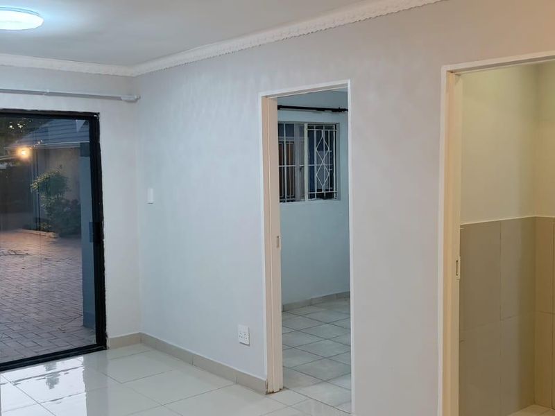An empty living area featuring tiled flooring, a sliding glass door with a security gate, and neutral wall finishes.