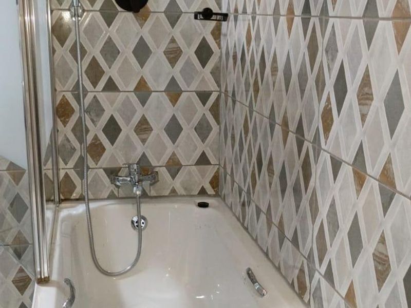 A clean bathroom featuring a built-in bathtub with a modern shower head, handheld shower attachment, and decorative diamond-patterned wall tiling.
