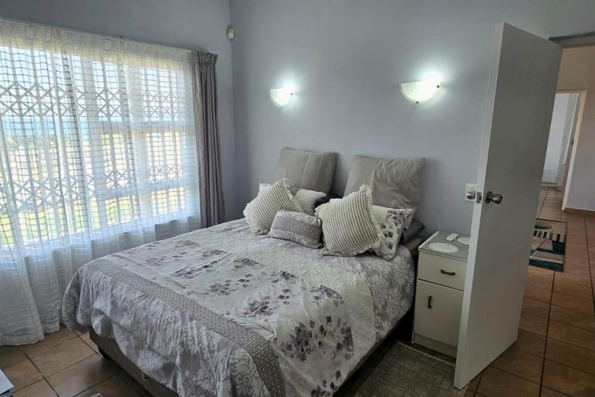 A bedroom featuring tiled flooring, wall-mounted lighting, and a large window with security gate, offering a view of the outdoors.