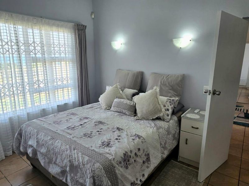 A bedroom featuring tiled flooring, wall-mounted lighting, and a large window with security gate, offering a view of the outdoors.