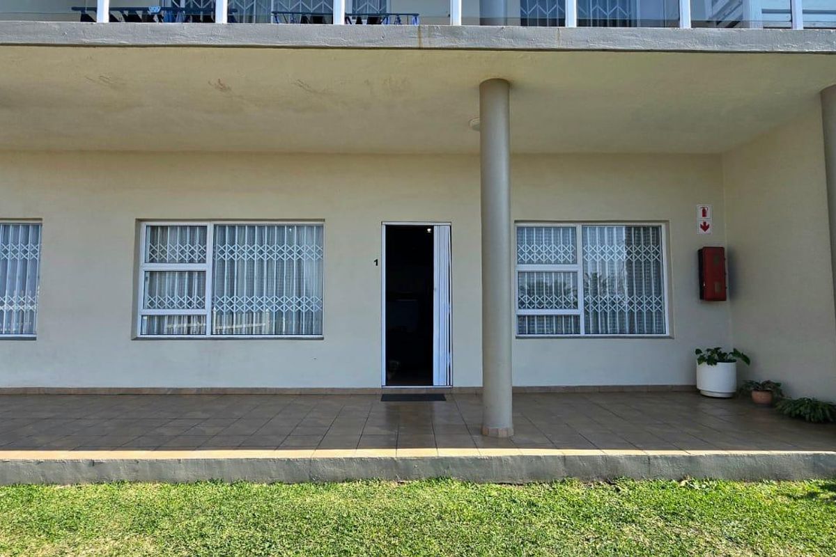Ground floor apartment exterior featuring a tiled patio, security gates on windows, and concrete support columns under an upper-level balcony.