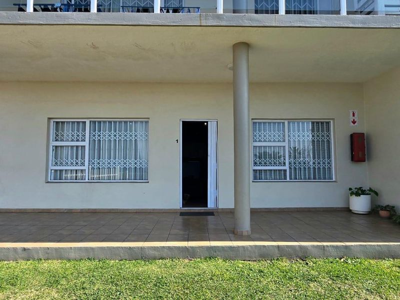 Ground floor apartment exterior featuring a tiled patio, security gates on windows, and concrete support columns under an upper-level balcony.