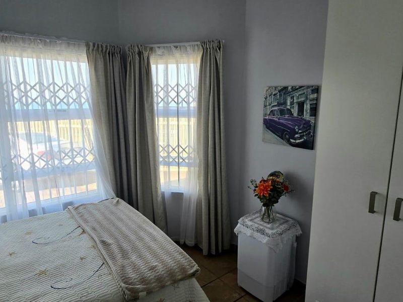 A bedroom featuring built-in wardrobes, tiled flooring, and large windows fitted with security gates for added safety.