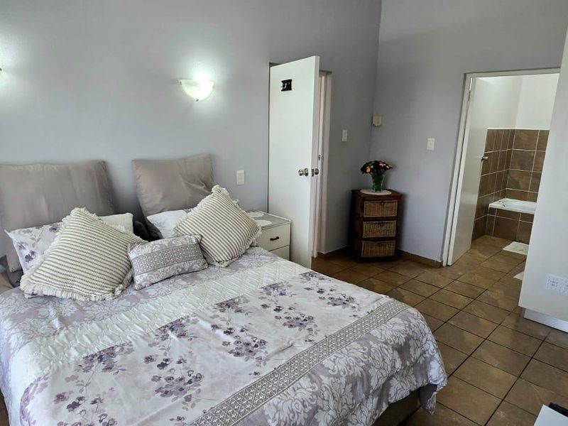 A bedroom featuring tiled flooring, built-in cupboards, and direct access to an en-suite bathroom with a bathtub.