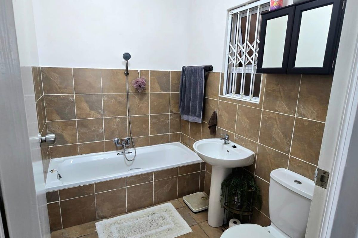 A functional bathroom featuring a bathtub with shower attachment, pedestal basin, toilet, and brown tiled wall finishes.