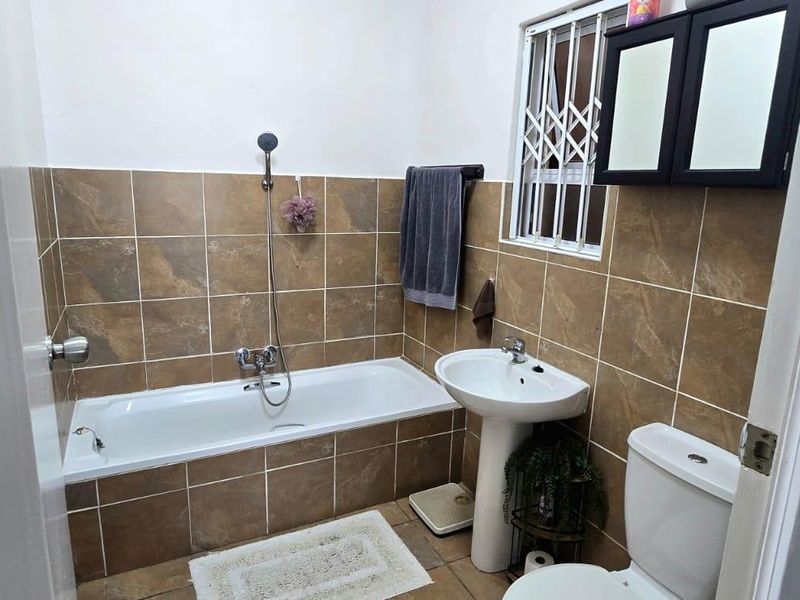 A functional bathroom featuring a bathtub with shower attachment, pedestal basin, toilet, and brown tiled wall finishes.