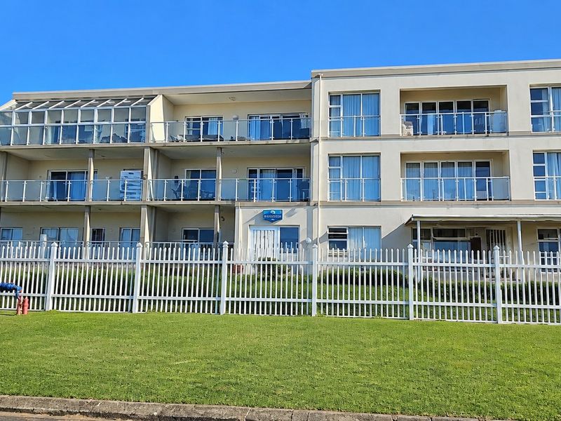 Front elevation of a multi-story apartment building featuring private balconies with glass balustrades and a well-maintained lawn area with a picket fence.