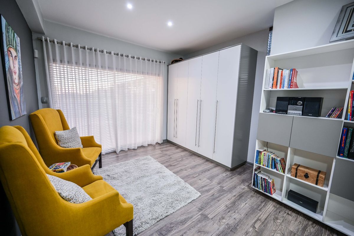 A well-maintained bedroom featuring modern laminate flooring, recessed downlighting, and a large white built-in wardrobe providing ample storage space.