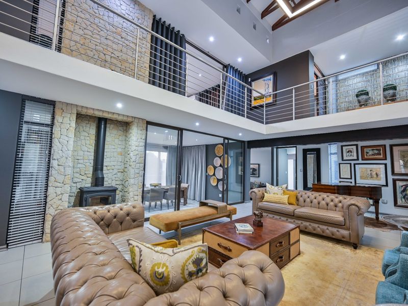 Spacious double-volume living area featuring a stone fireplace, mezzanine level with stainless steel balustrades, exposed timber rafters, and large sliding doors to the patio.