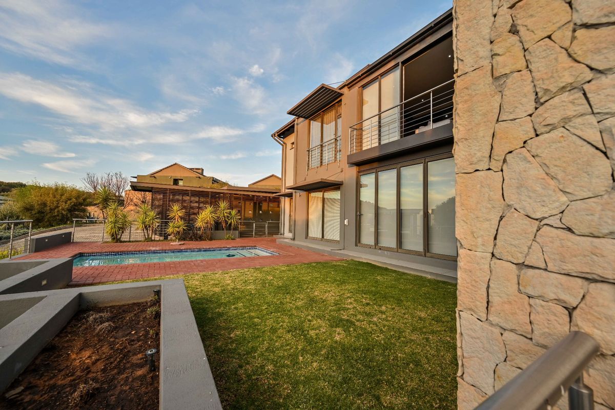 Rear exterior view featuring a swimming pool, landscaped garden, stone-clad feature wall, and a multi-level dwelling with balcony and sliding glass doors.