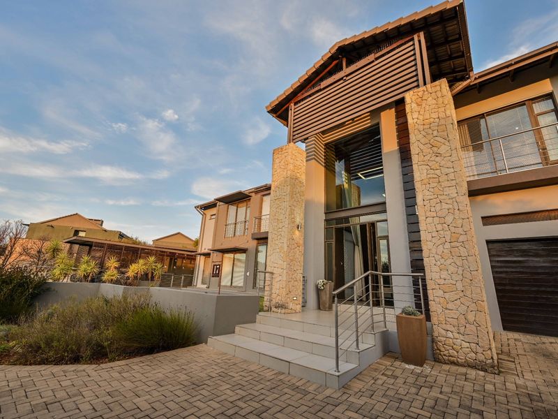 Modern double-storey residence featuring stone-clad pillars, a paved driveway, and a prominent entrance with stainless steel balustrades.