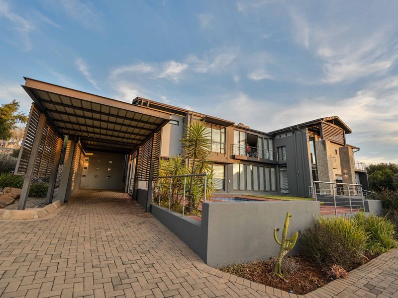 Modern multi-story residence featuring a spacious carport, stone-clad architectural details, a private balcony, and a front-facing swimming pool area.