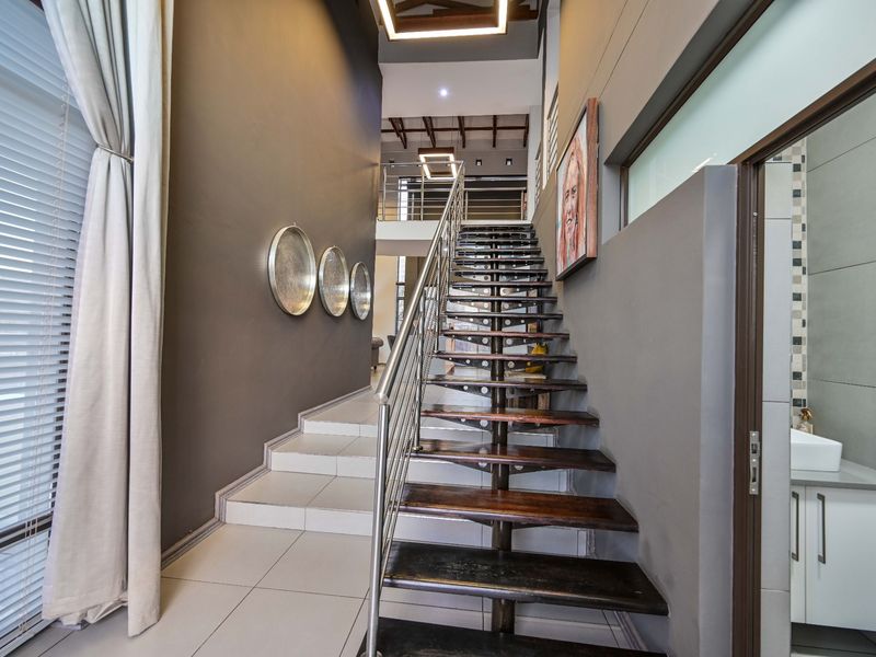 Modern hallway featuring a striking timber and stainless steel staircase, tiled flooring, and a convenient adjacent vanity area with contemporary finishes.
