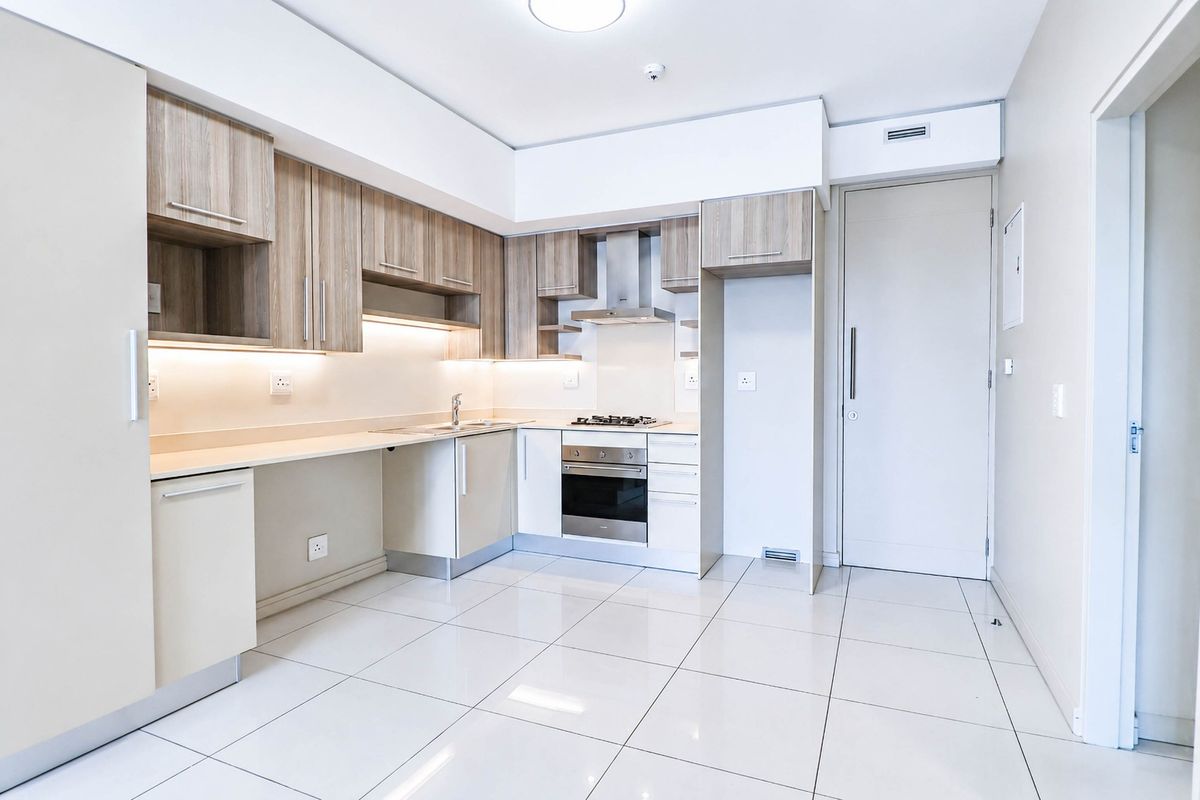 Modern kitchen featuring light wood-tone cabinetry, integrated stainless steel appliances, under-cabinet lighting, and sleek tiled flooring in a clean, minimalist layout.
