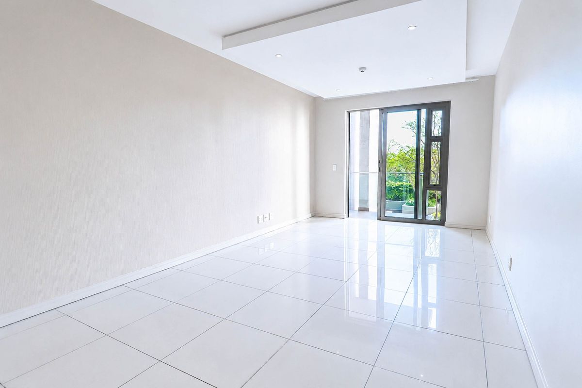 A bright, empty living room featuring polished porcelain floor tiles, a modern recessed ceiling with downlights, and a sliding glass door leading to a balcony.