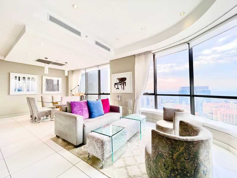 A bright and modern open-plan living and dining area featuring floor-to-ceiling windows with expansive city views, recessed lighting, and sleek tiled flooring.
