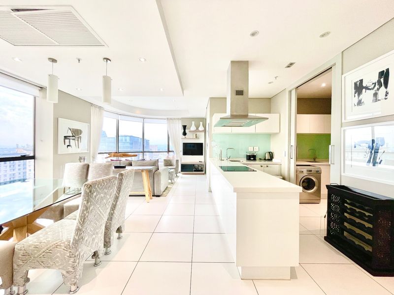 Modern open-plan apartment featuring a sleek kitchen with island, integrated appliances, and a seamless flow into the dining and living areas with floor-to-ceiling windows.