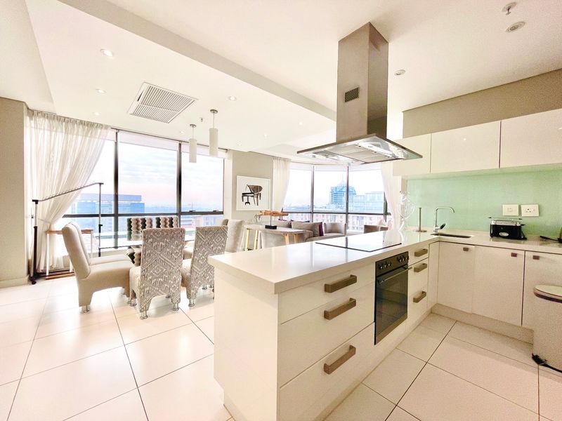 Modern open-plan kitchen and living area featuring high-end finishes, a central island with built-in appliances, and expansive floor-to-ceiling windows with city views.