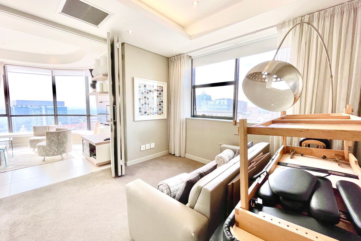 A bright, modern living area featuring carpeted floors, recessed ceiling lighting, and a folding partition leading to an adjacent sunroom with expansive city views.