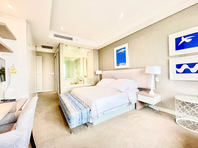 Modern bedroom featuring neutral textured wallpaper, recessed lighting, ducted air conditioning, and a sleek glass-enclosed en-suite bathroom.