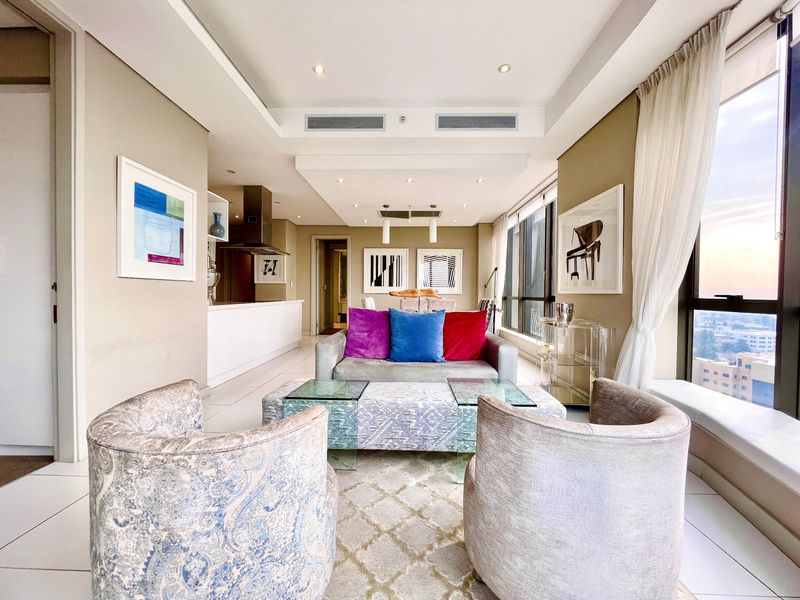 Modern open-plan living area featuring tiled floors, recessed ceiling lighting, ducted air conditioning, and expansive floor-to-ceiling windows with integrated kitchen space.