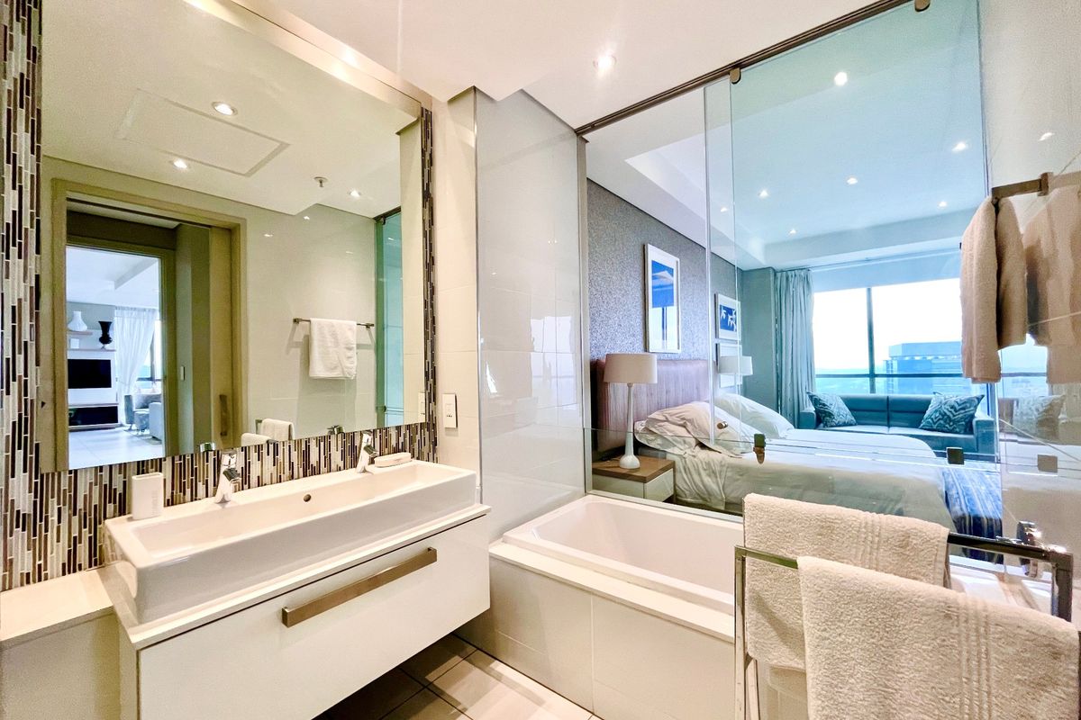 Modern en-suite bathroom featuring a wall-mounted vanity, integrated basin, and a glass partition wall overlooking the adjacent bedroom.