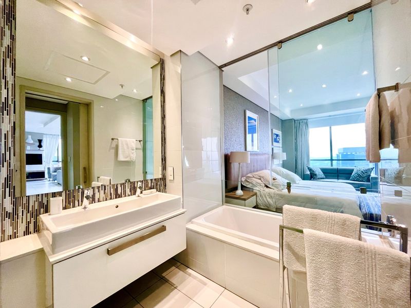 Modern en-suite bathroom featuring a wall-mounted vanity, integrated basin, and a glass partition wall overlooking the adjacent bedroom.