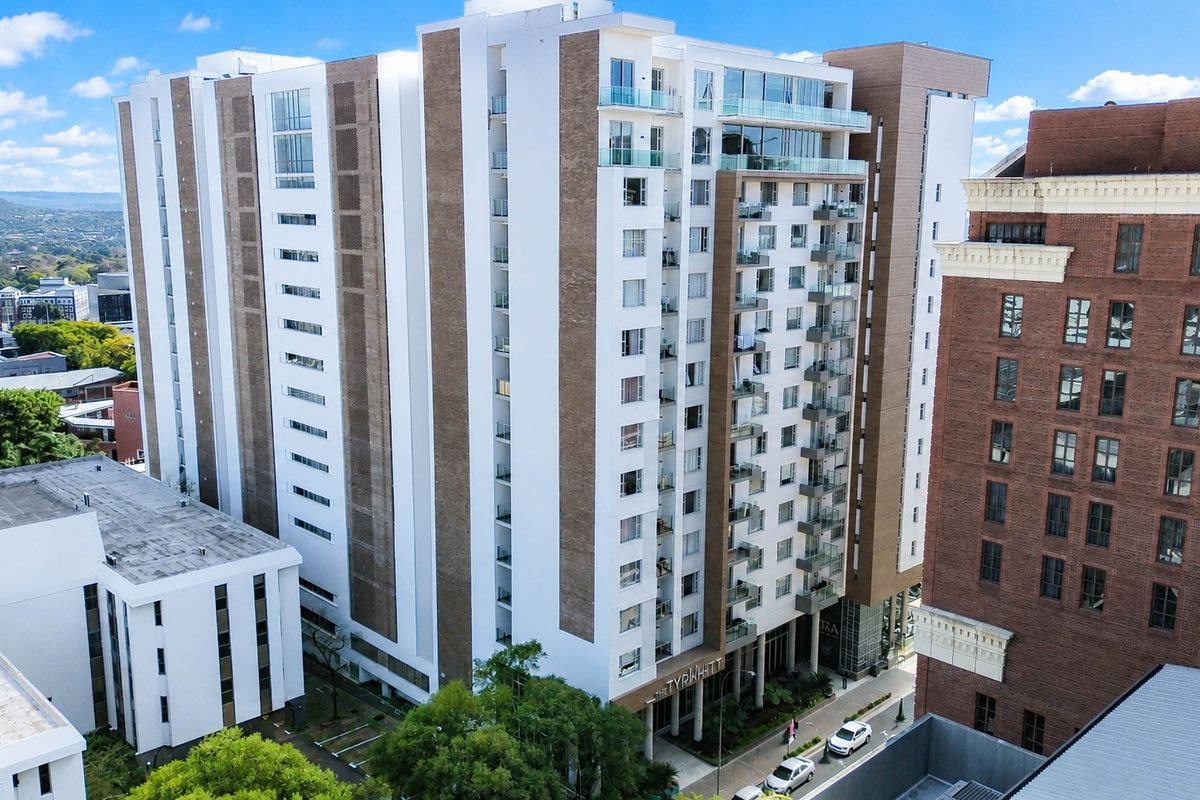 Aerial view of a modern multi-story apartment complex featuring contemporary architectural design, glass balconies, and a prominent ground-level entrance.