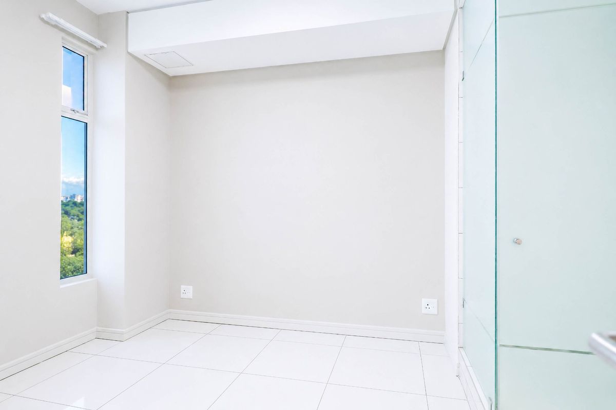 A bright, empty bedroom featuring clean white tiled flooring, a large window with a view, and a modern glass partition wall.