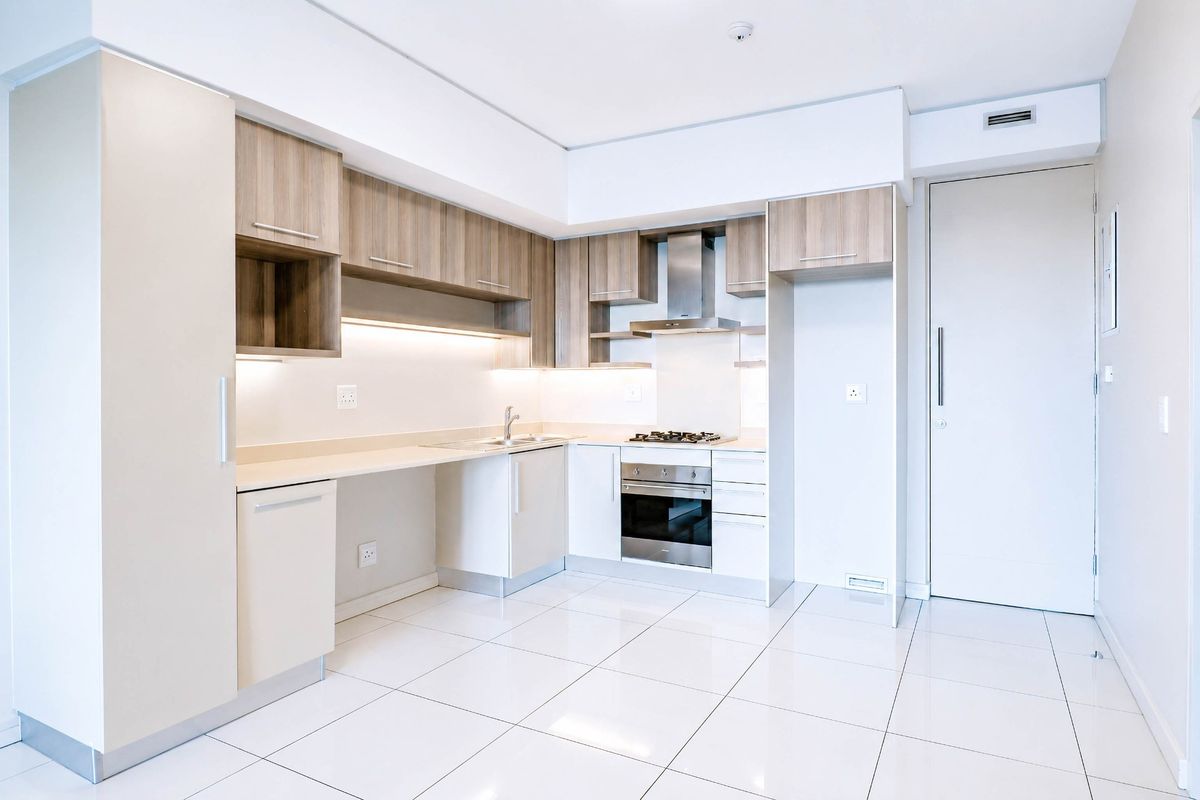 Modern kitchen featuring sleek wood-tone cabinetry, stone countertops, integrated stainless steel appliances, and polished white floor tiles in a clean, minimalist layout.
