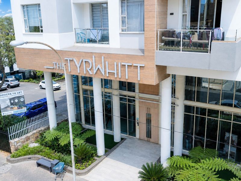 Aerial view of the modern apartment building entrance, featuring glass facade, stone cladding, and balconies with glass balustrades.