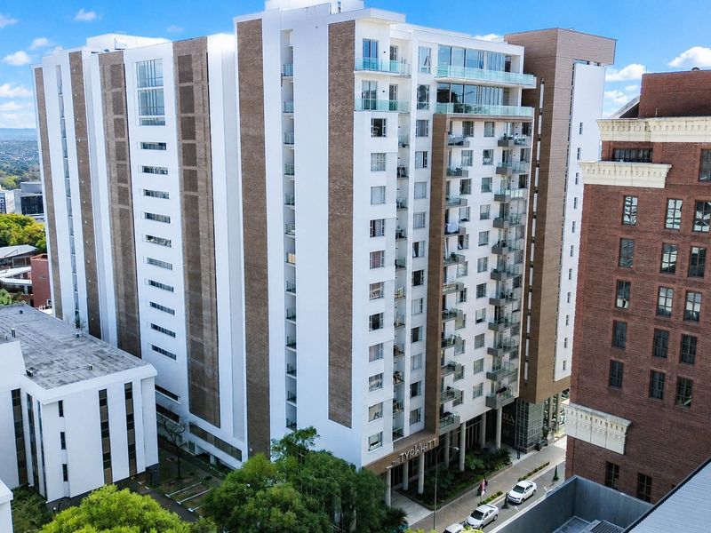 Aerial view of a modern multi-story apartment complex featuring contemporary architectural design, glass balconies, and a prominent ground-level entrance.
